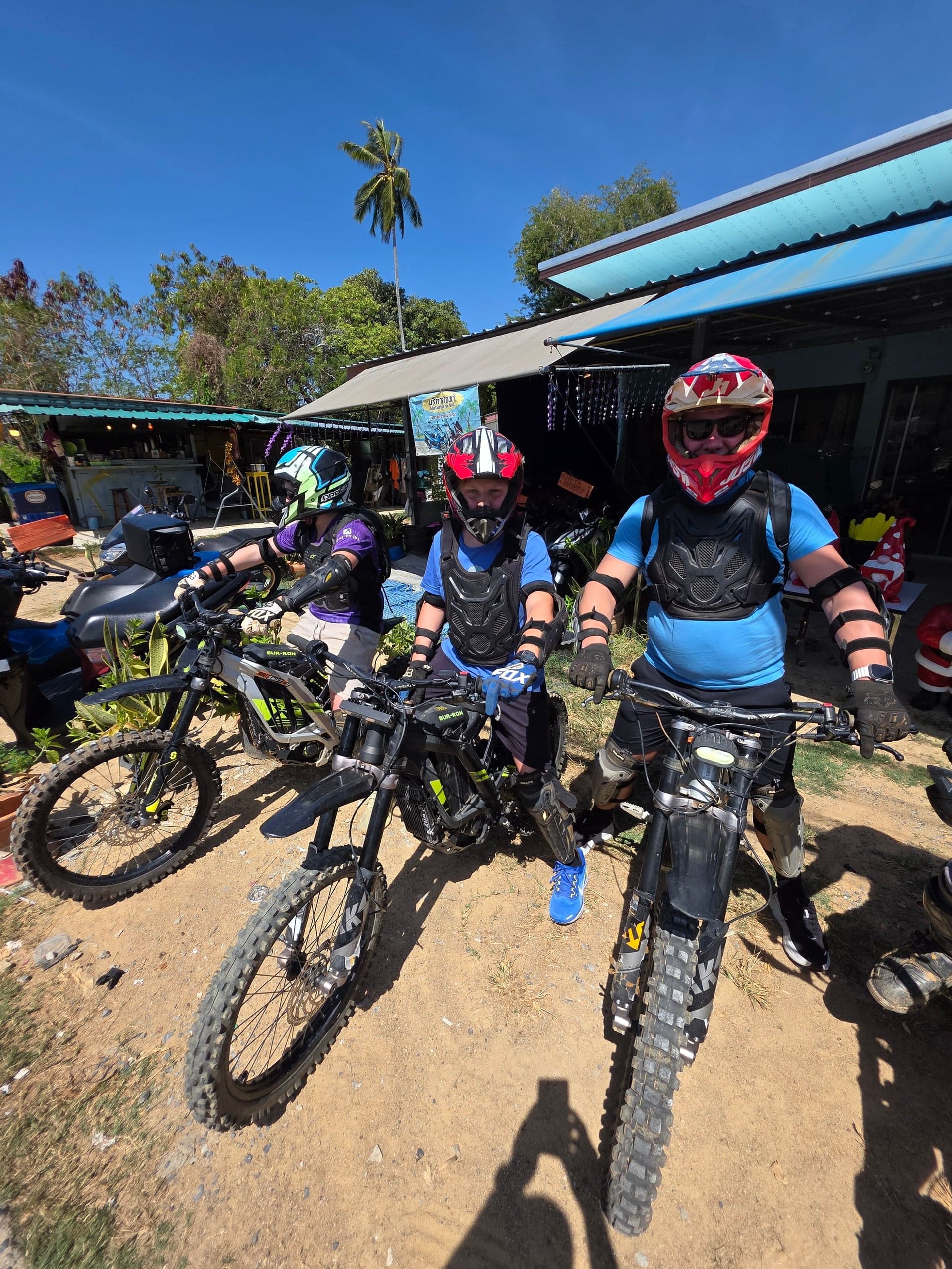 Three people on electric motorbikes in Phuket, Thailand, ready for a tour under a clear blue sky.