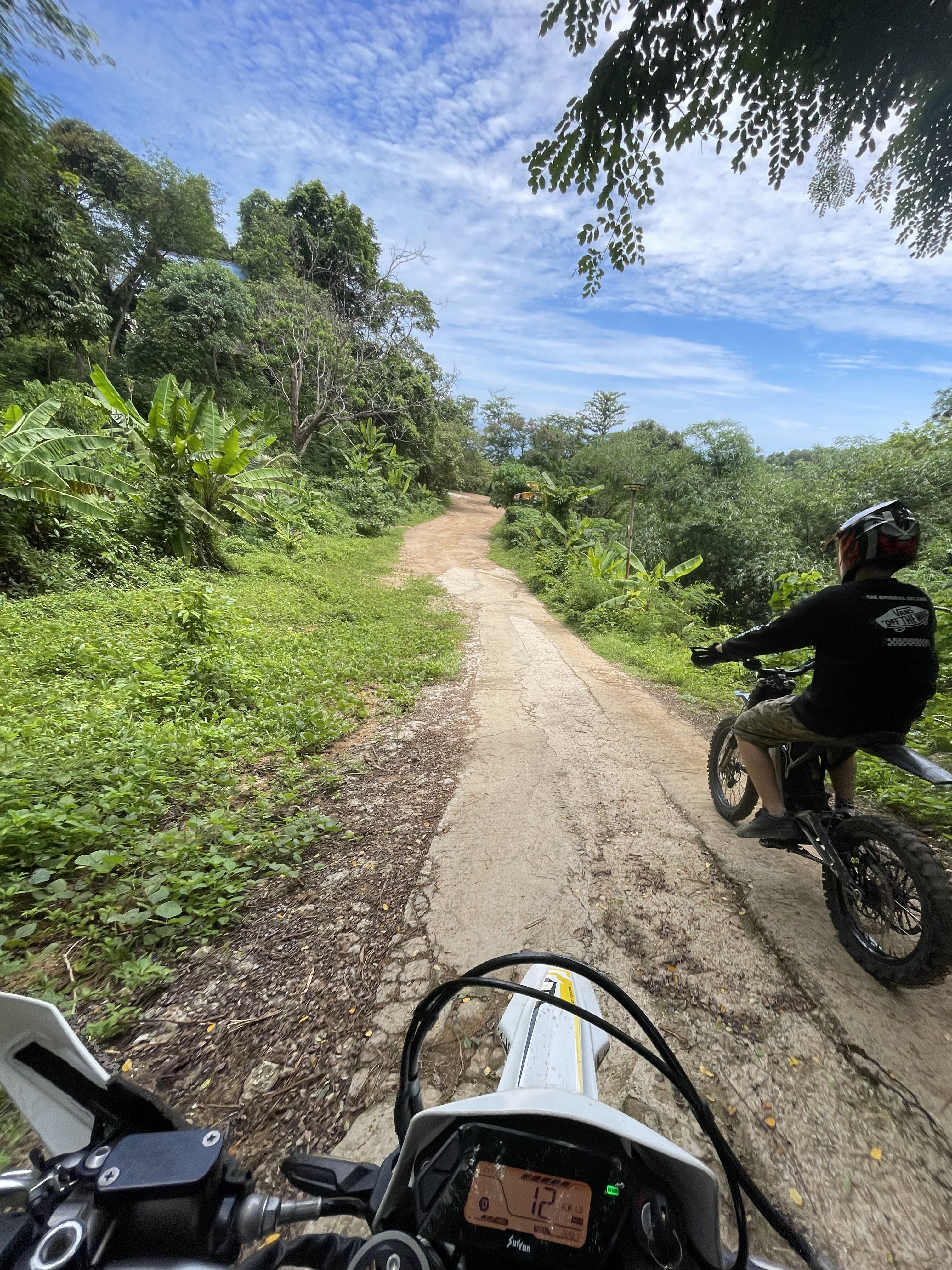A Surron electric motorbike tour participant riding through a scenic, green forest trail in Phuket, Thailand.